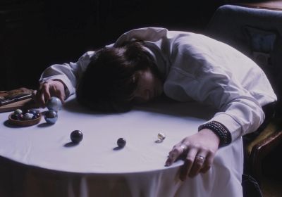 Film still from 'Stiltes' (2024) by Jon Beaton. A teenage student sits at a round table with her head against its surface, surrounded by marbles arranged from small to large.